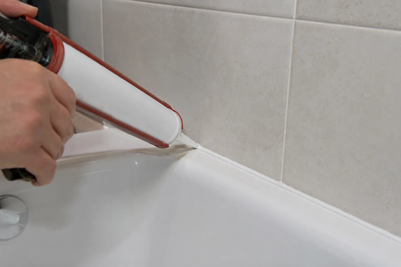 Nakładanie białego silikonu sanitarnego pistoletem przy krawędzi wanny i płytek łazienkowych